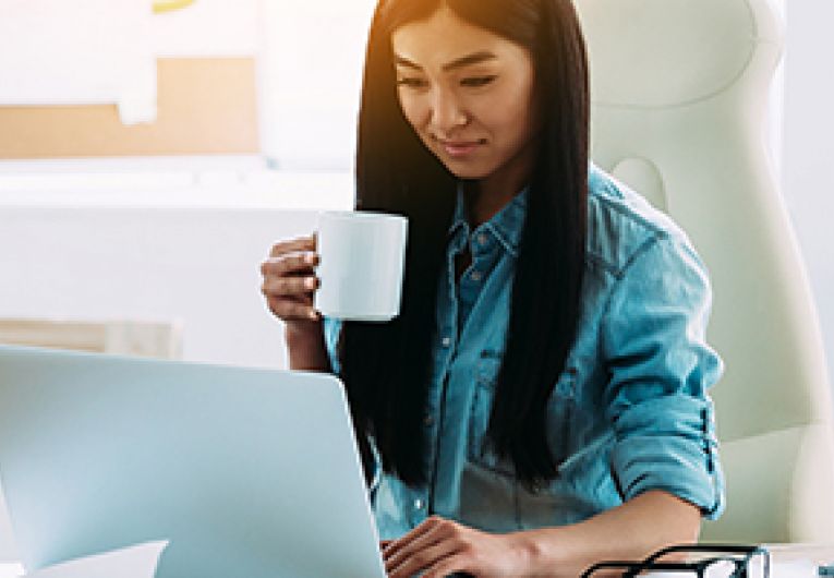 Entrepreneur works in front of a laptop while holding a mug in her hand.