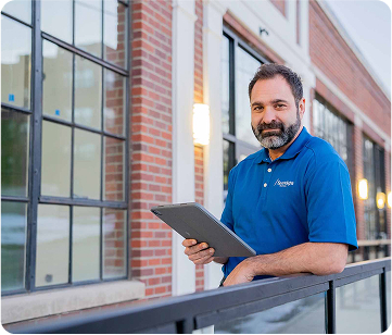 Sparklight tech in a blue branded shirt with a tablet standing outside of a brick business building