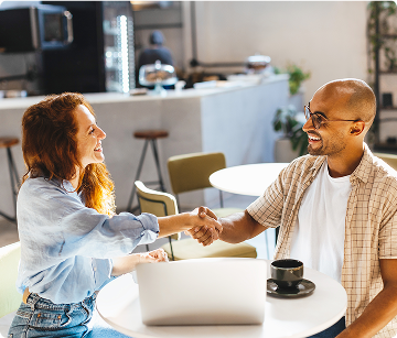 A woman and man seated at a cafe shaking hands