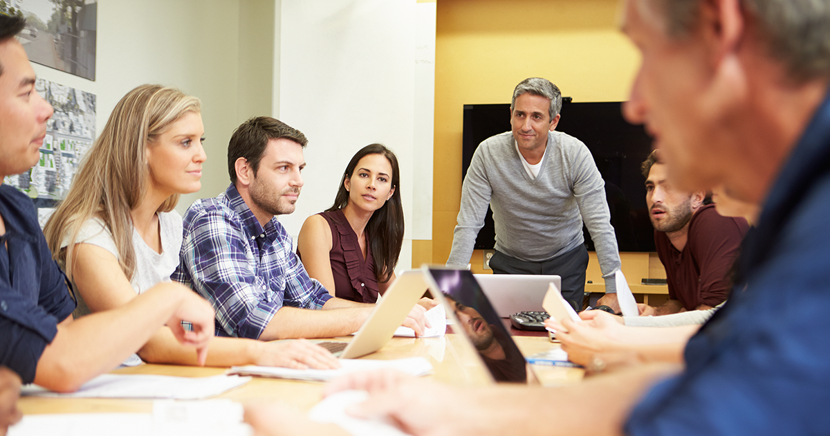 Mature businessman addressing employees or board members in meeting around boardroom table