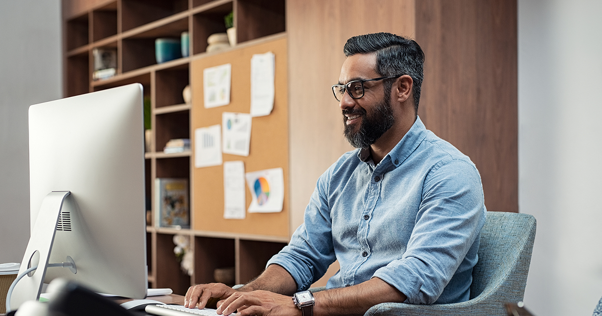 Smiling creative businessman typing on desktop computer in office.