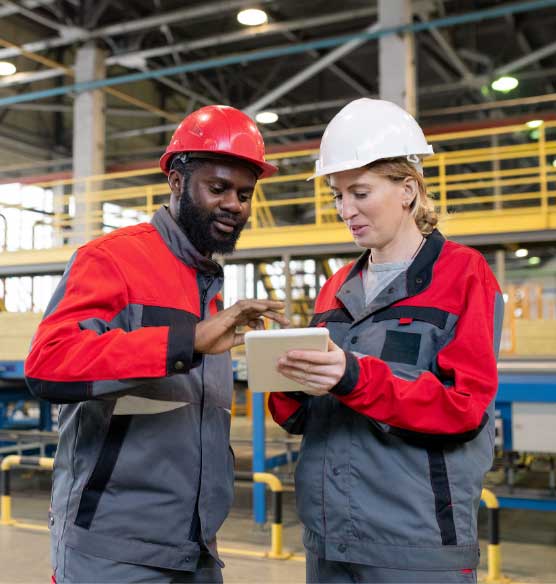 Man and woman in a warehouse wearing hard hats looking at a tablet screen