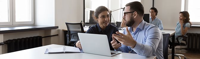 Two business professionals talking while sitting at a desk.