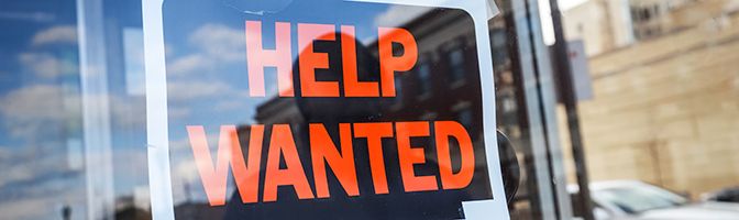 Close up of a help wanted sign in the window of a business.
