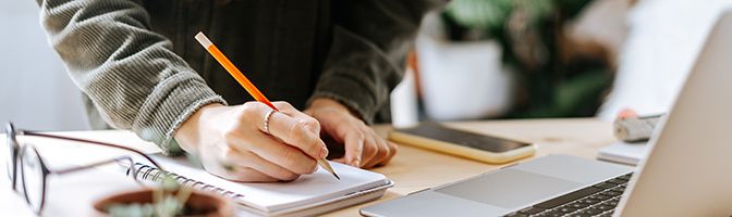 Close up of business owner writing on a notepad in front of a laptop.