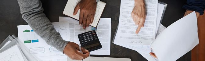 close up of people using a calculator over a paper strewn desk