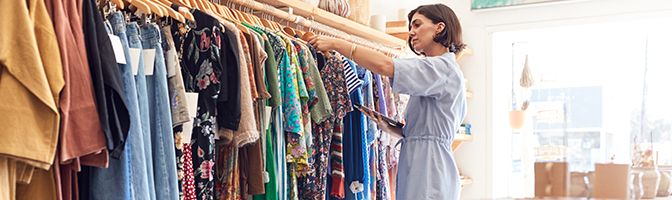 Small business owner checks back-to-school clothing inventory in her store with tablet device.