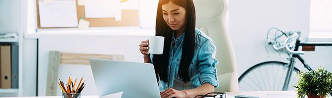 Entrepreneur works in front of a laptop while holding a mug in her hand.