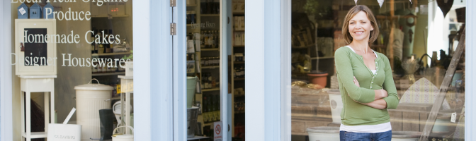 Woman working in local shop standing in front of store front 