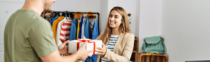 Young shopkeeper giving gift to customer at clothing store.