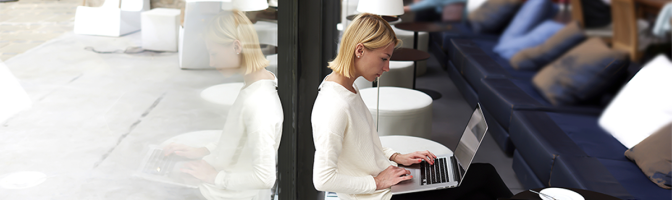 Female student connecting to wireless via laptop computer while sitting in modern coffee shop or university library