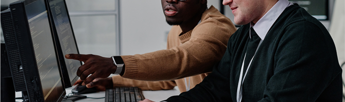 Programmer pointing at computer monitor with codes and talking to his colleague while they working with computer program in team