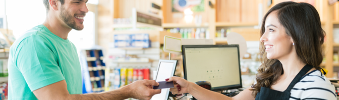 Smiling female cashier with buyer at checkout counter in grocery store