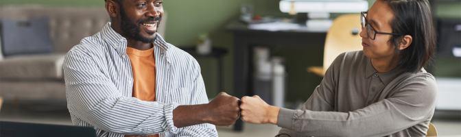 Two businessmen fist bumping while working together in office