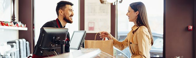 A small business owner smiles as he hands over a shopping bag to the customer at the register.