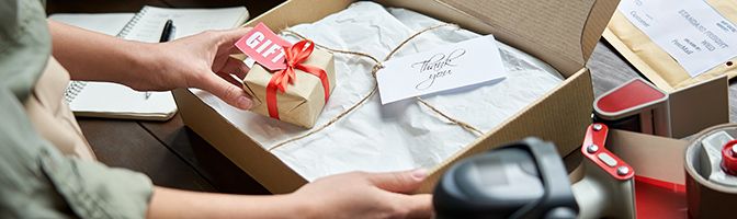 Business person prepares gift wrapped purchase for shipping in a box.