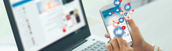 A person holds a smartphone that has social media icons floating through the screen.