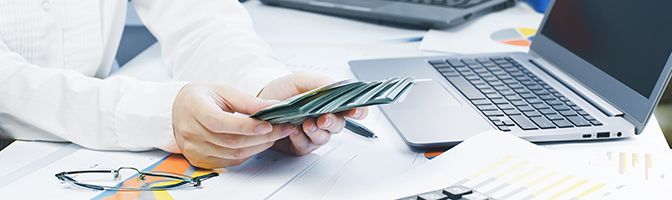 A person holding money in front of a laptop.