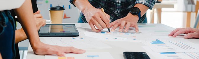 Close up of three business professionals around a table covered with print outs.