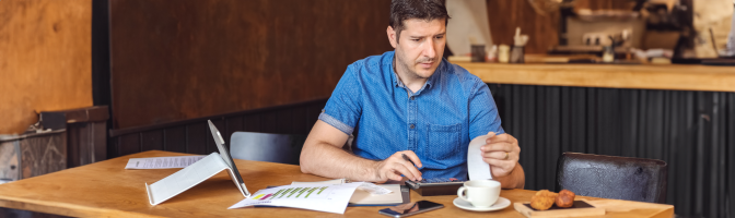 Male restaurant owner sitting at table while reviewing budget.