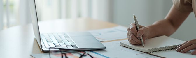 Small business owner writing on a notepad while looking at a laptop.