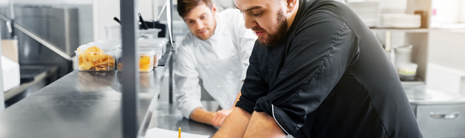 happy male chef and cook with grocery lists or bills at restaurant kitchen