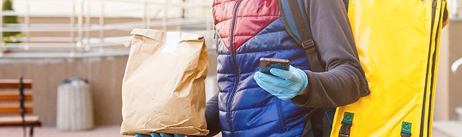 Delivery person looking at a mobile device while holding a large brown bag.