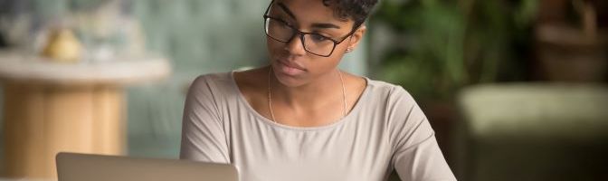 Woman taking notes while viewing a laptop