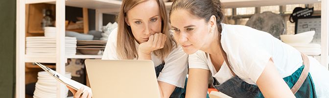 Two women entrepreneurs look at a laptop screen together.