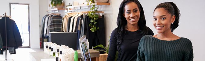 Two business owners smile while at the cash register in a store.