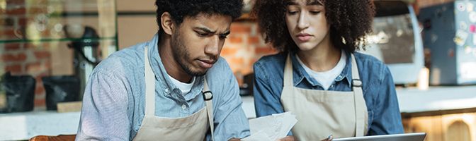 Two business owners of a coffee shop look over financial statements.