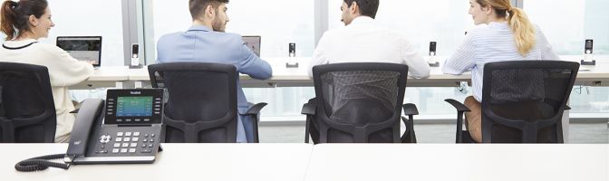 Business professionals sitting in conference room with desktop phone sitting on table.