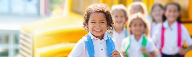 smiling young kids in front of school bus 