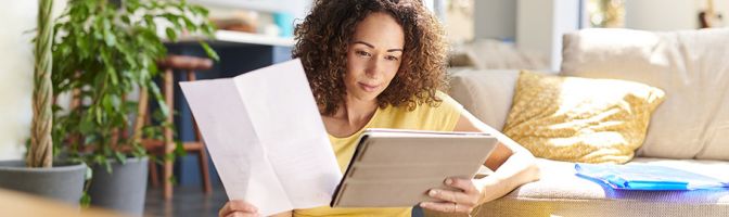 woman comparing the information on a piece of paper to a tablet