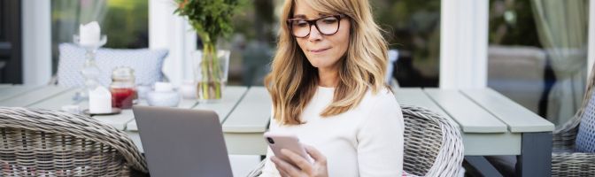 middle age woman works from her pack yard on laptop and phone