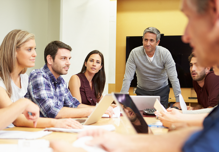 Mature businessman addressing employees or board members in meeting around boardroom table