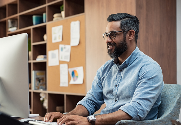 Smiling creative businessman typing on desktop computer in office.