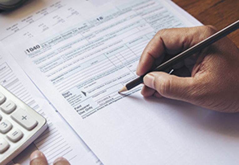 Close up photo of business person filling out a tax form with a calculator next to it.