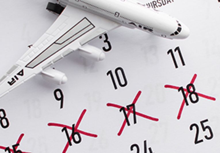 Vacation concept with calendar marked off with a red pen surrounded by a toy airplane and sunglasses.
