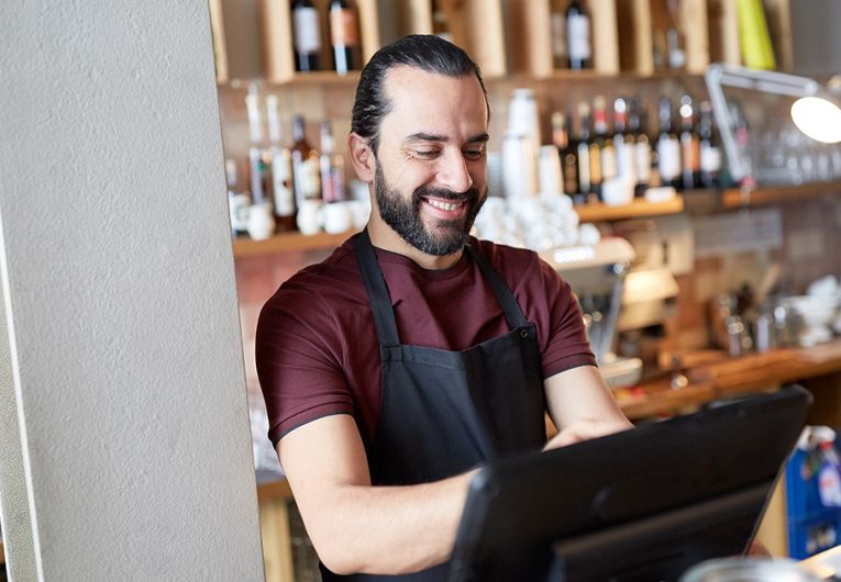 small business owner in apron at counter working at bar or coffee shop on computer