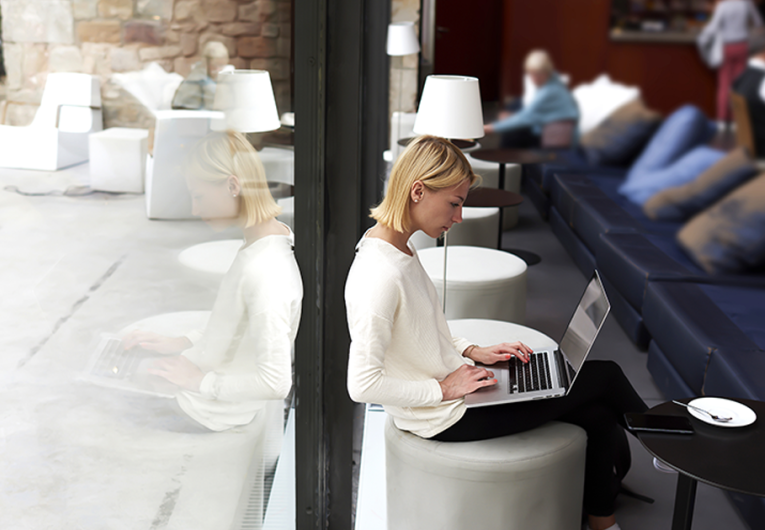 Female student connecting to wireless via laptop computer while sitting in modern coffee shop or university library