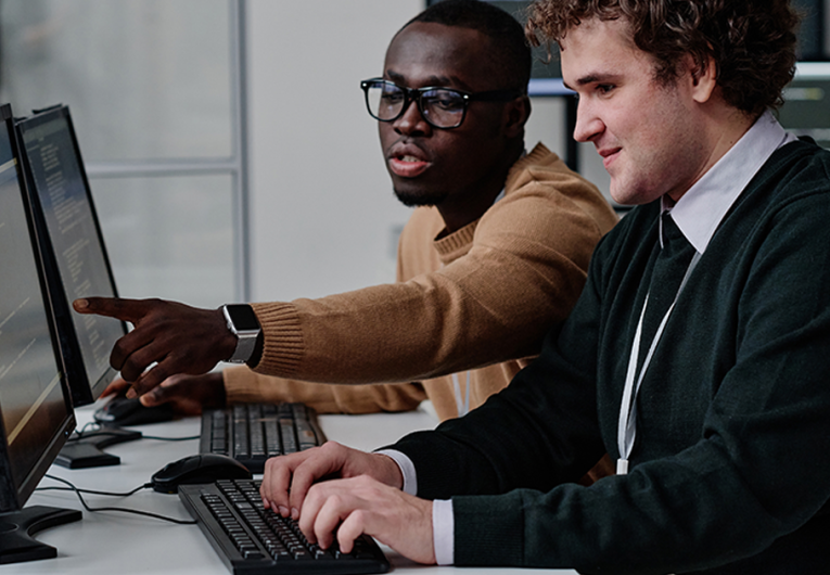 Programmer pointing at computer monitor with codes and talking to his colleague while they working with computer program in team