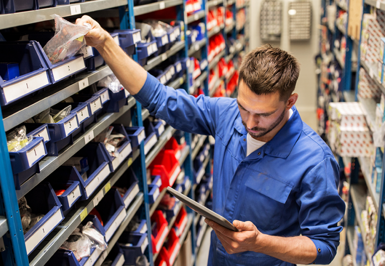 Auto mechanic with tablet computer looking for parts at workshop or warehouse.