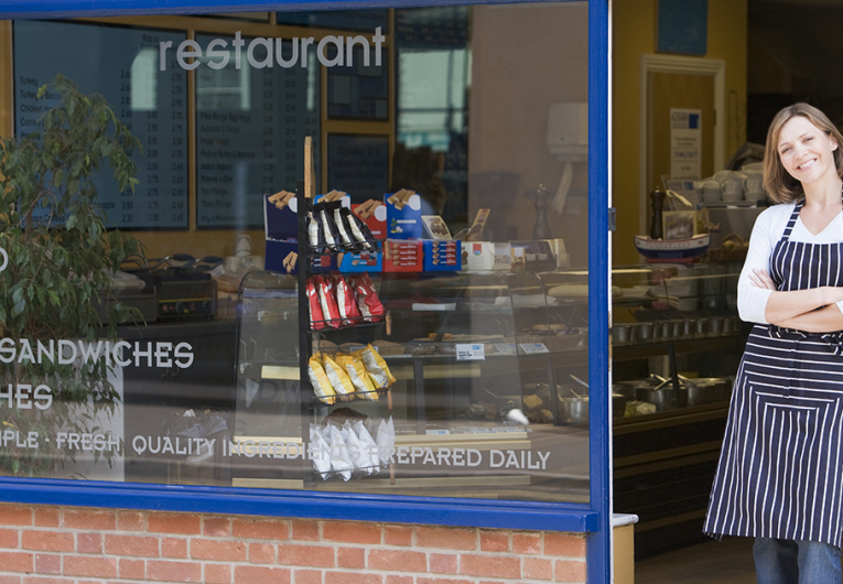 Female business owner, shop worker, standing in front of restaurant storefront. 