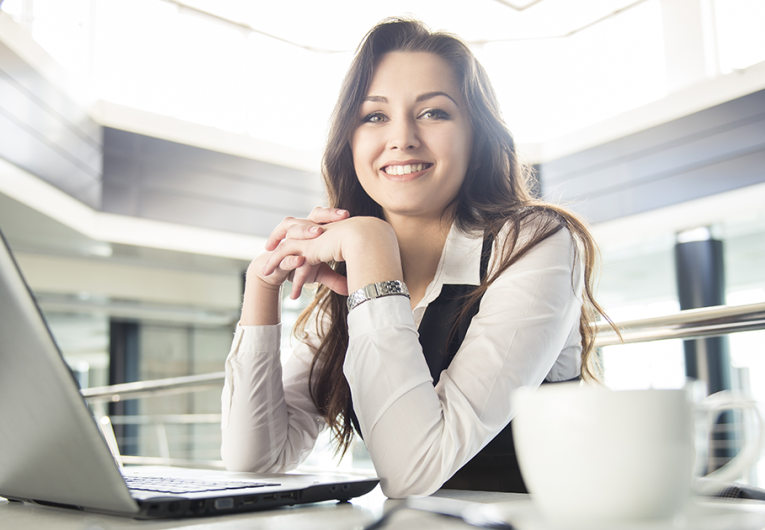 Smiling young business woman working for a laptop in a modern office.