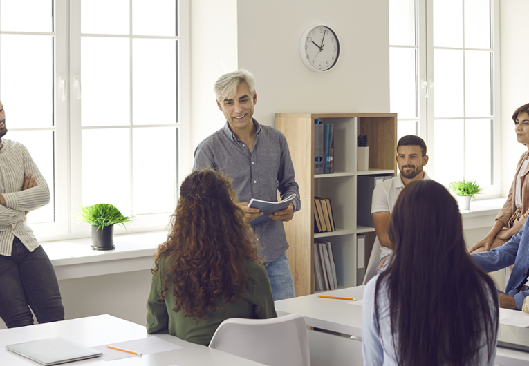 Team of people listening to senior business coach during training meeting in office