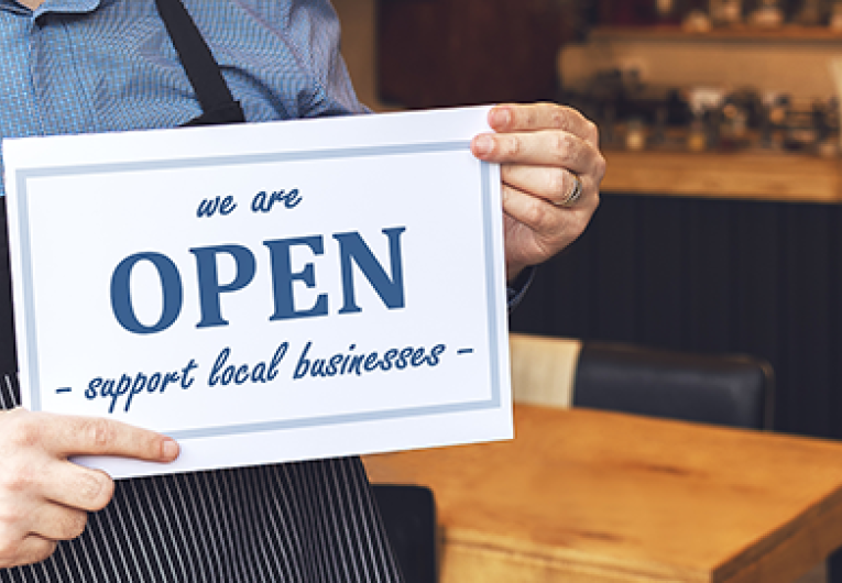 Small business owner smiling while holding open sign of restaurant