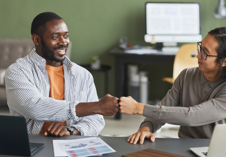 Two businessmen fist bumping while working together in office