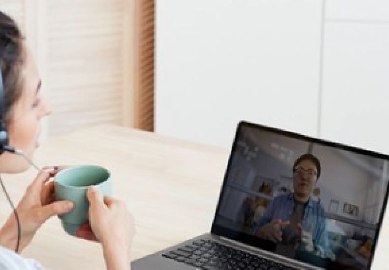 Woman holding a cup and wearing headphones while on a video conference call