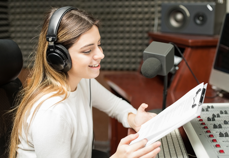 Woman with clipboard in hand sitting in soundproof room at radio station and hosting a talk show live